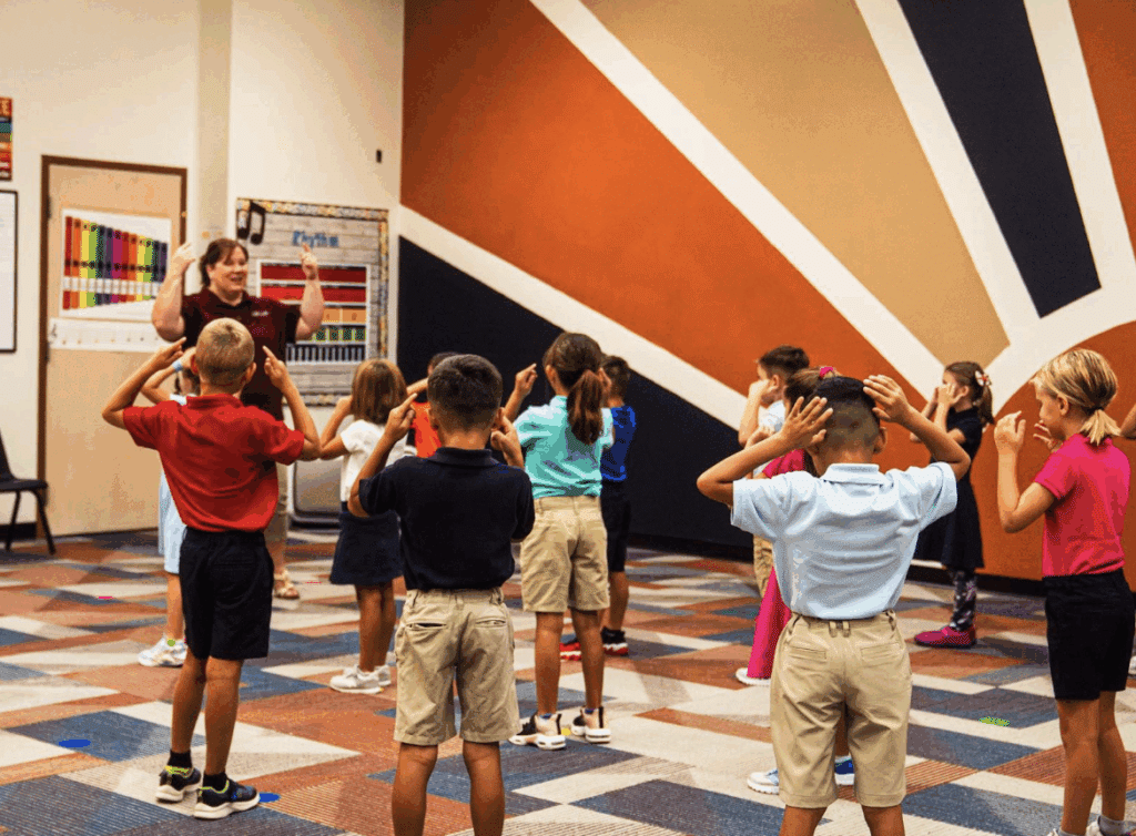 Teacher standing in front of a group of students all with their hands held to their heads