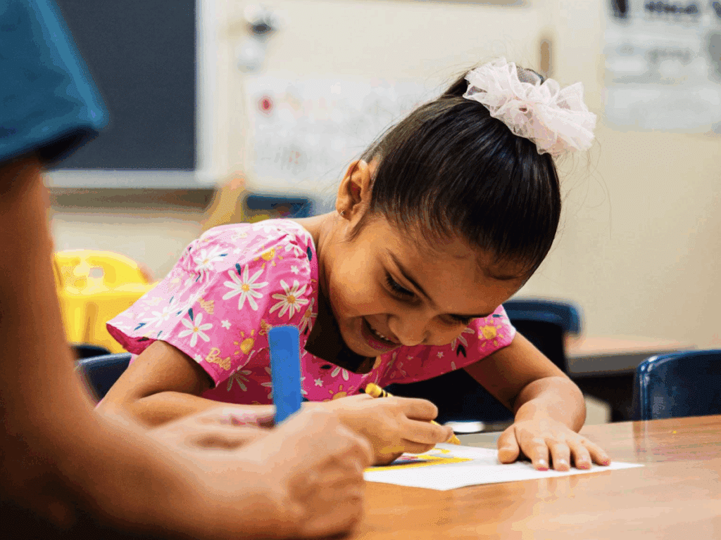 Girl drawing with crayons in classroom setting